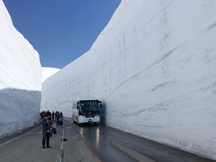 Bus driving through massive snow walls on a mountain road