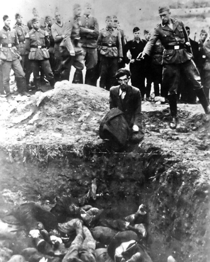 Creepy historical photo showing a man kneeling by a mass grave surrounded by soldiers