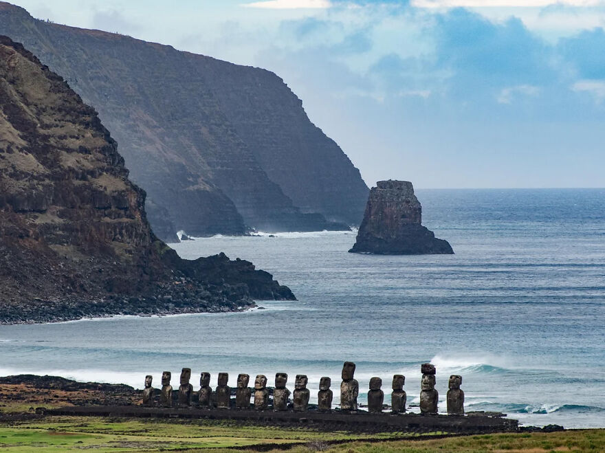 Moai statues stand on a rocky coast with dramatic cliffs and an isolated stack in the Pacific Ocean, epitomizing isolated places.