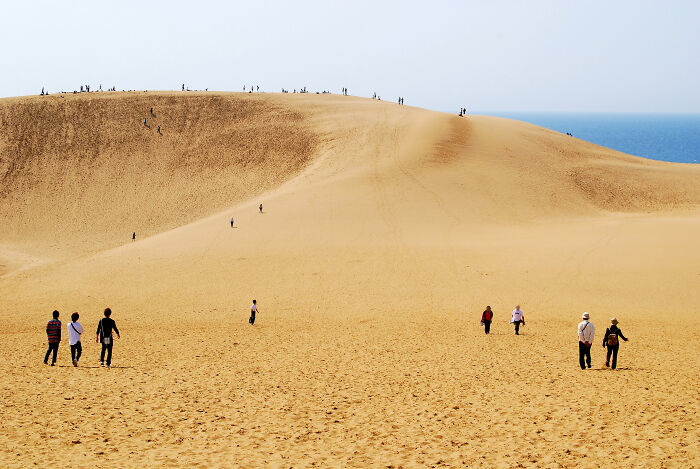 People walking up large sand dune under clear sky with stunning desert views