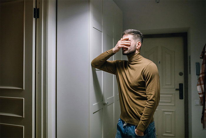 Man stressed holding face indoors near door, reflecting on difficult family issue