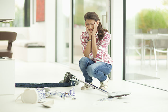 Woman upset witnessing broken vase while cleaning broken ceramic pieces on floor