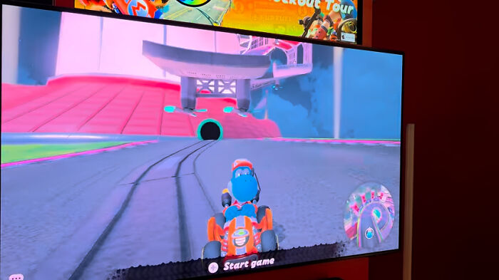 A blue character in an orange kart on a vibrant race track, ready to start a game. Epic comebacks in gaming!