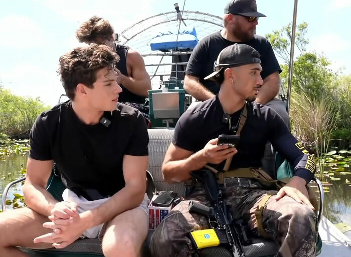 Looksmaxxing influencer and armed friend riding on a boat in a swamp
