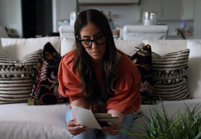 A woman with glasses and an orange shirt looks through old photos, reflecting on Michael Jackson accusations and 60 Minutes interview.
