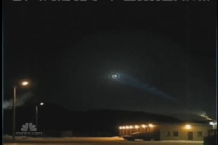 Night sky with mysterious glowing spiral light above buildings