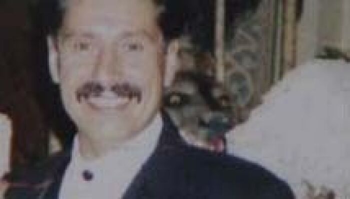 Smiling man with mustache and a strange figure in background odd bench photo