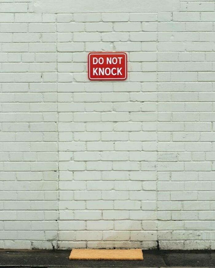 Do not knock sign mounted on unremarkable white brick wall