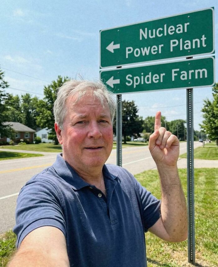 Man pointing at road sign showing directions to nuclear power plant and spider farm