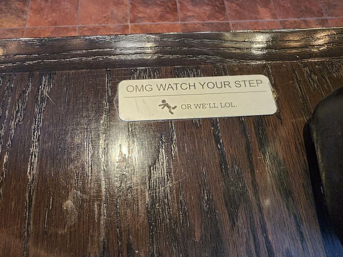 Humorous caution sign on floor saying watch your step or we'll laugh