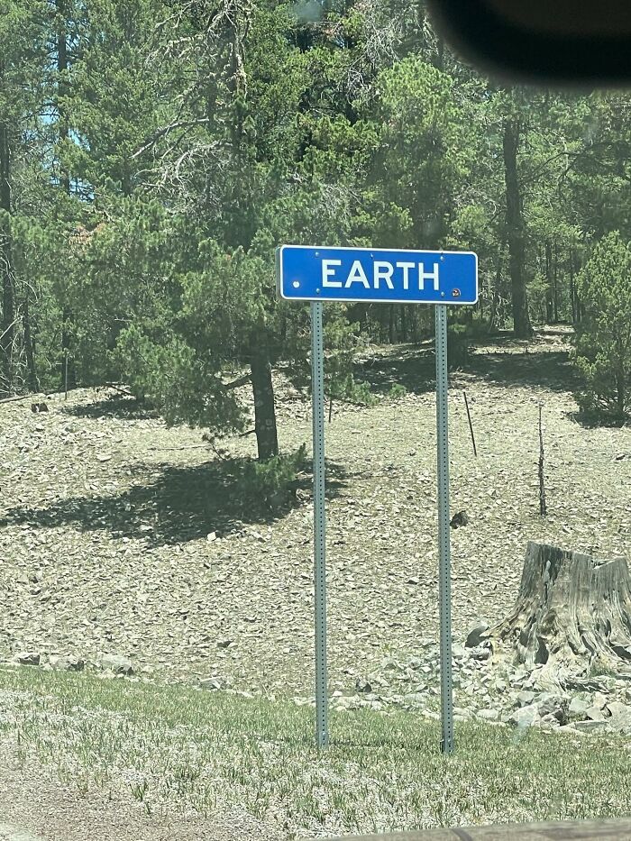 Blue road sign for town or location named Earth surrounded by trees