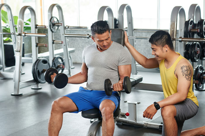 Two men working out together with dumbbells inside gym Two men working out together with dumbbells inside gym