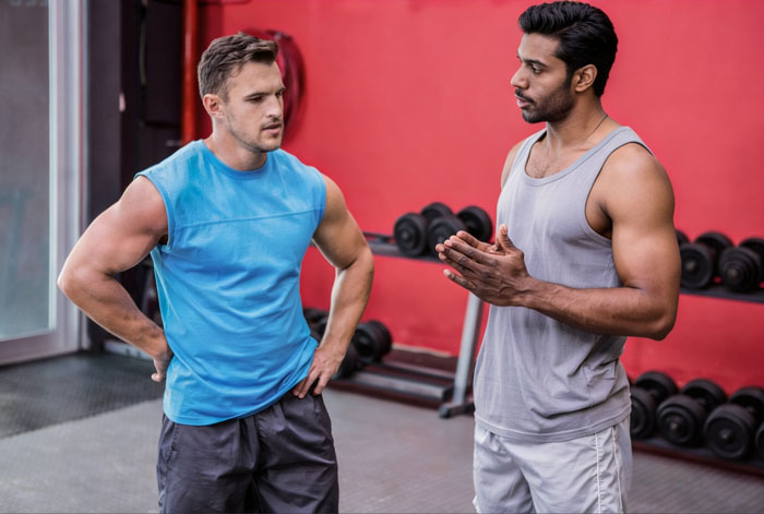Two men talking in gym with dumbbells in background gym setting Two men talking in gym with dumbbells in background gym setting