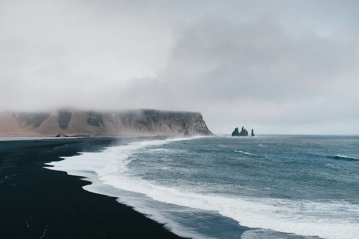 Black sand beach with cliffs and ocean waves on a foggy day geography fact