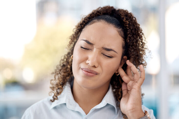 Woman with curly hair grimacing and touching her ear, indicating discomfort. Important for routine cancer screening.