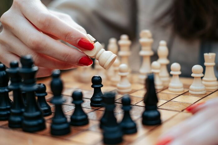 A person's hand with red nail polish moves a white chess piece, showing a fascinating strategy in play.