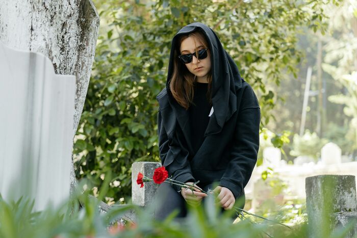 Young woman in black with red flowers sitting contemplative in a cemetery
