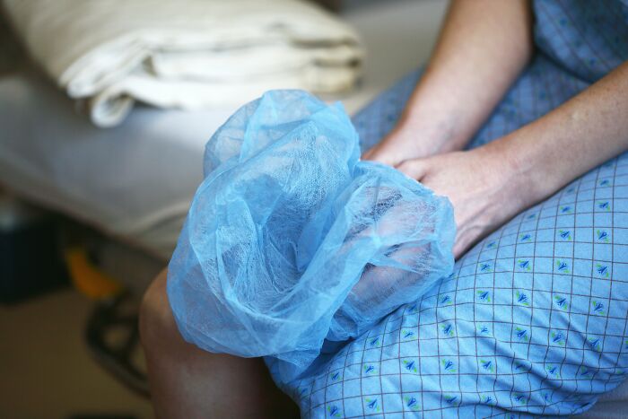 A person in a hospital gown holding a blue surgical cap, contemplating creepy things.