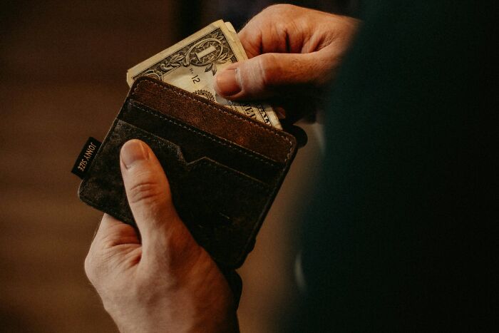 Hands putting a dollar bill into a brown wallet, hinting at rich people's silent luxuries.