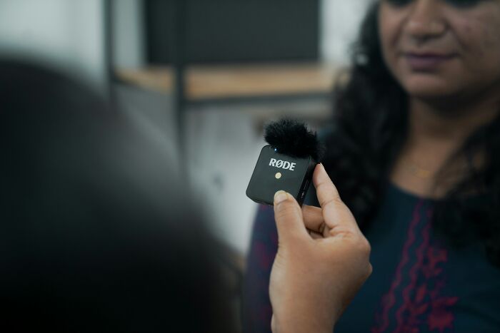 A hand holds a RØDE microphone, recording a woman. Capturing Gen Z content for digital natives.