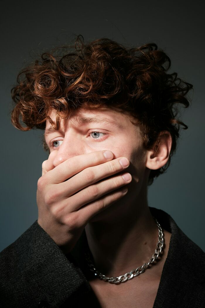 A young person with curly brown hair covers their mouth, looking away with wide blue eyes. Disturbing d***h stories.