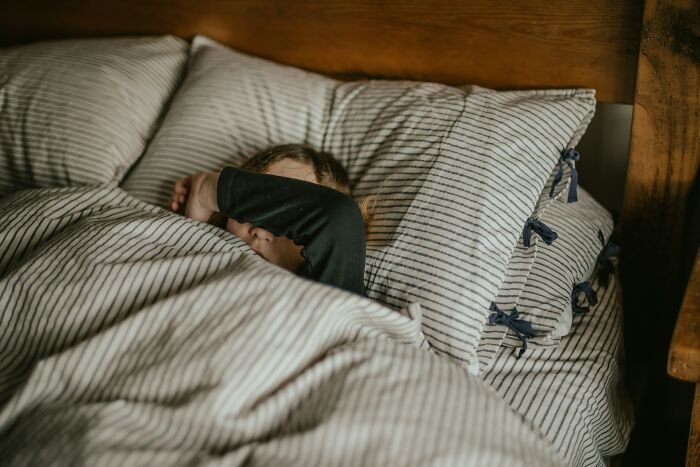Child resting in bed with striped bedding, unrelated to poverty meals