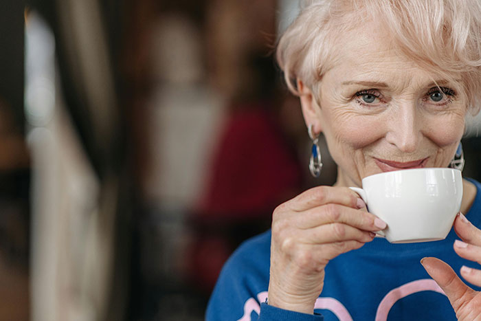 Smiling senior woman with pink hair enjoying a cup of tea. She could be a MIL creating chaos.