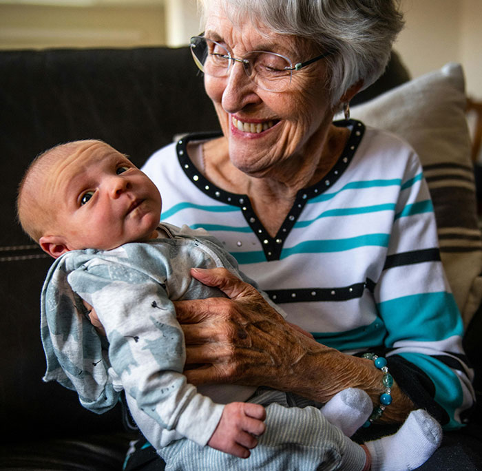 A smiling grandma with glasses holds a newborn, reflecting the loving side of MILs. No chaos here.