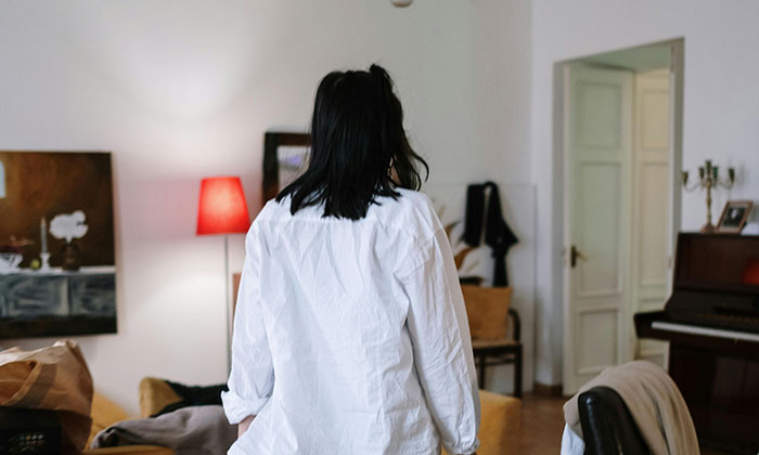 A woman in a white shirt stands in a living room, back to the camera. This image explores MILs creating chaos.