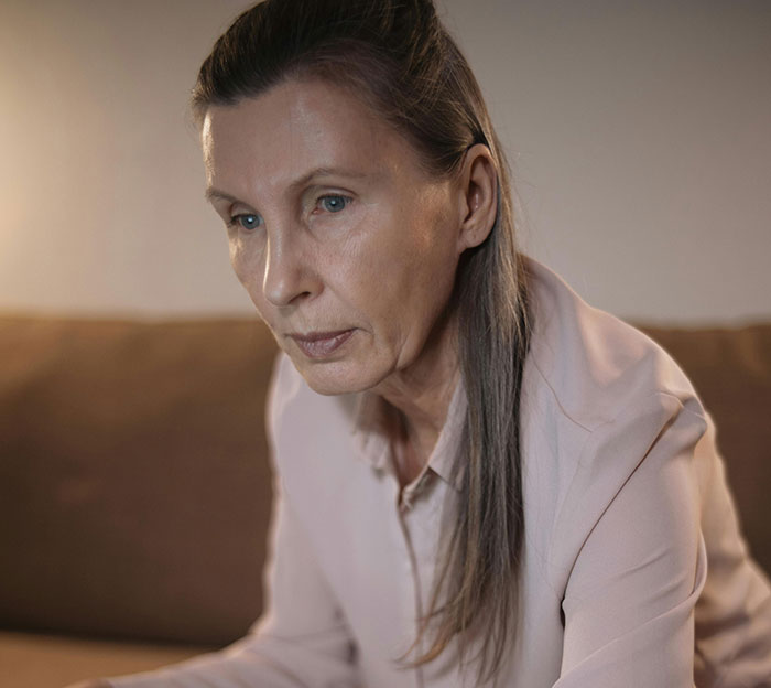 A middle-aged woman with blue eyes and graying hair, looking downcast. This image relates to MILs creating chaos.