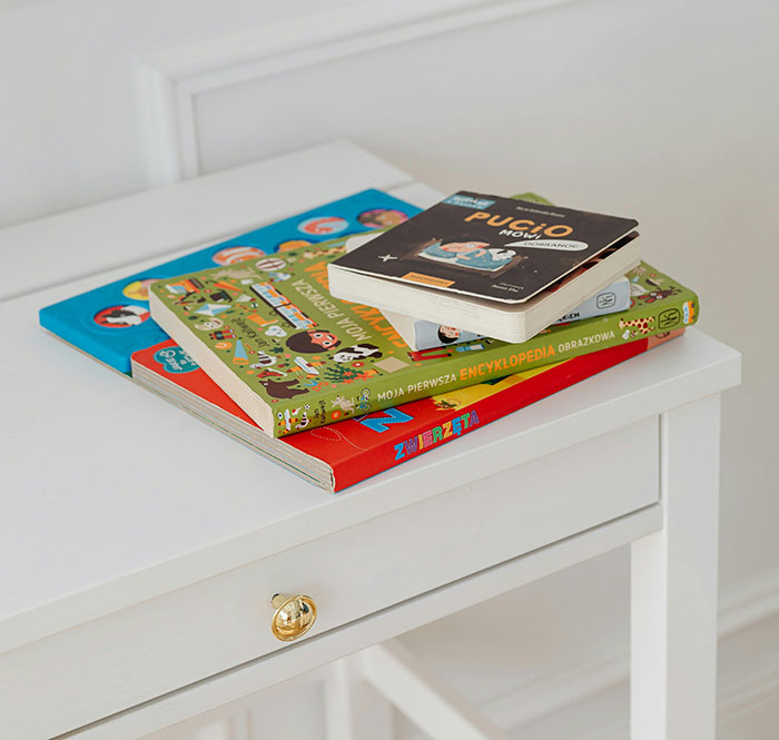 A stack of colorful children's books on a white nightstand. MILs often create chaos; these books offer an escape.