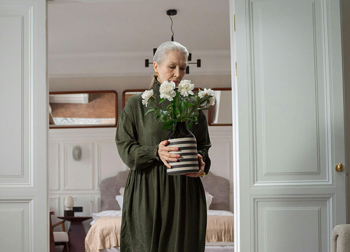 A woman in a green dress holding a vase of white flowers, possibly a MIL, contributing to family chaos.