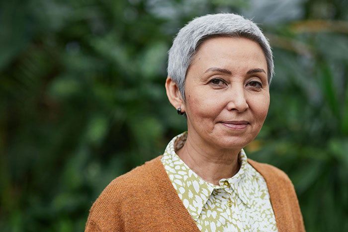 A smiling woman with short gray hair and an orange cardigan, looking directly at the camera, exemplifying MILs.