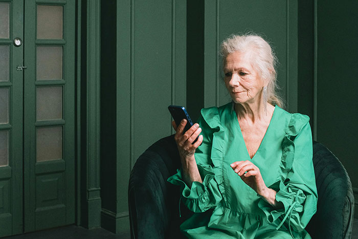 A white-haired MIL wearing a green dress, looking at her phone, possibly creating chaos with a text.