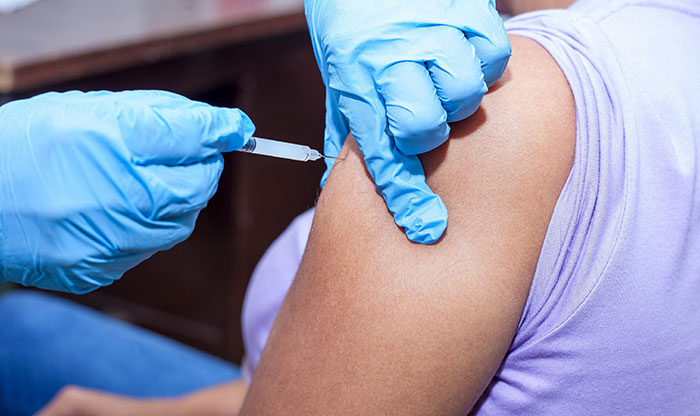 A nurse in blue gloves administers a vaccine to a patient's arm, similar to MILs creating chaos.