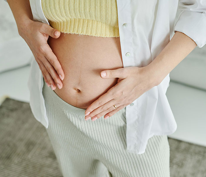 Pregnant woman in a yellow top and white shirt, cradling her belly. MILs can create chaos during pregnancy.