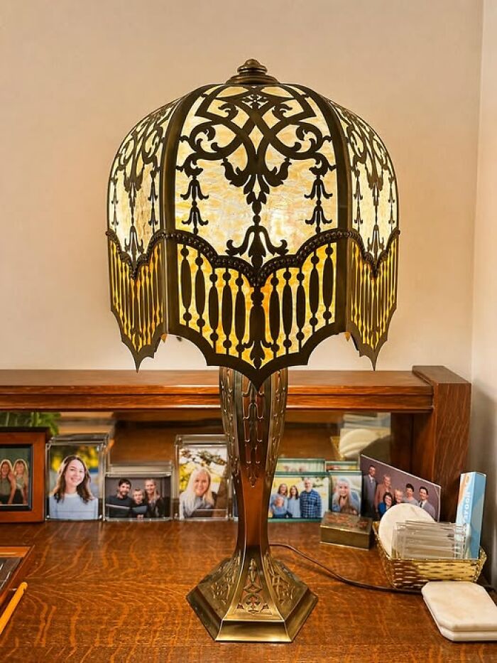Antique brass lamp with decorative domed shade on wooden desk surrounded by photos