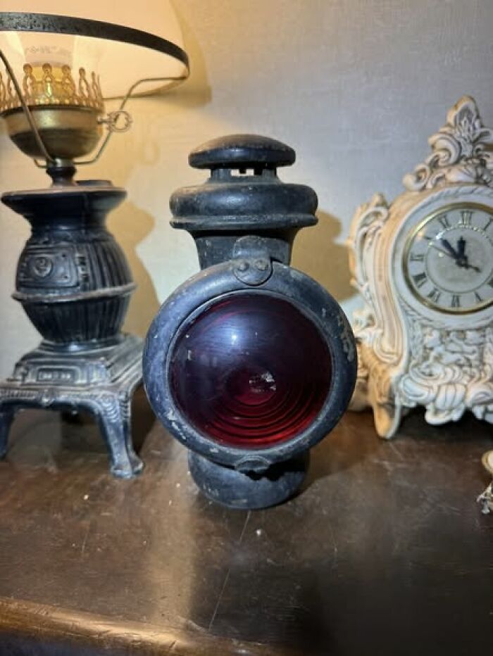 Old-fashioned black metal oil lamp with red glass lens next to antique clock