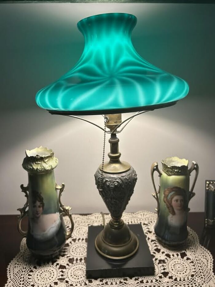 Vintage secondhand lamp with glowing turquoise shade and ornate metal base on lace tablecloth