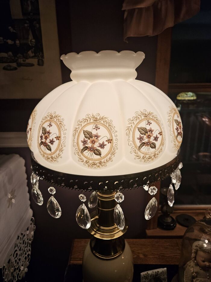 Antique floral painted glass lamp with hanging crystal drops illuminated in dim room