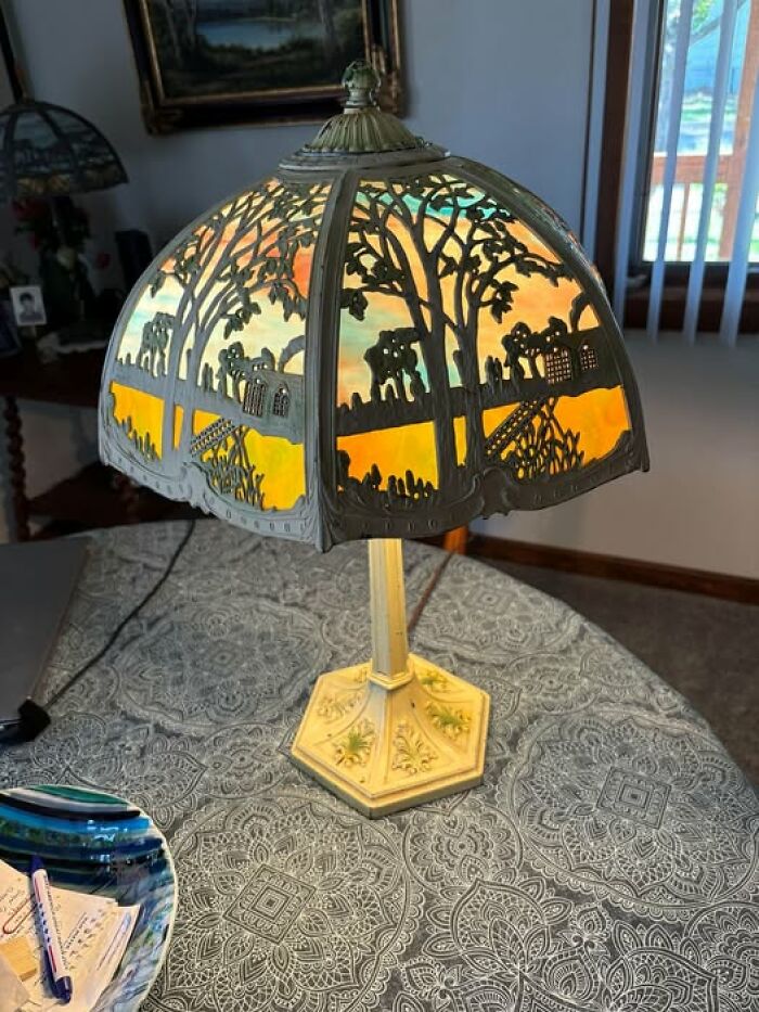 Vintage secondhand lamp with intricate cutout shade and illuminated base on patterned tablecloth
