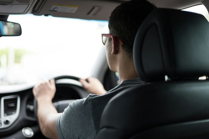 A man with glasses and a gray shirt driving a car, a common scenario where doctors might ask, "How the hell are you even alive right now?"