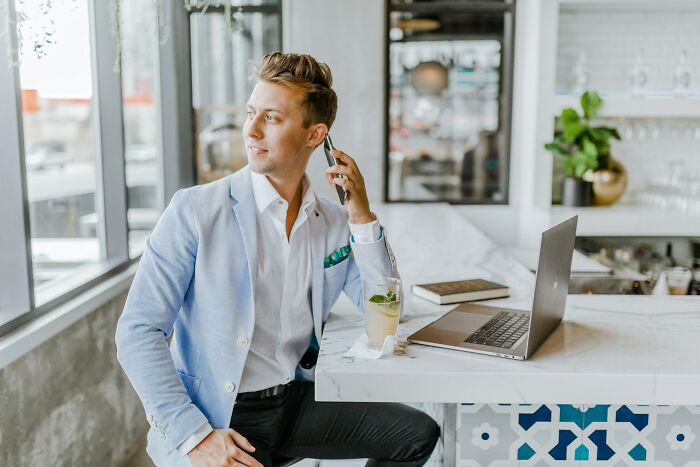 Young man in light blue jacket using phone by a laptop, revealing industry secrets of Googling skills.