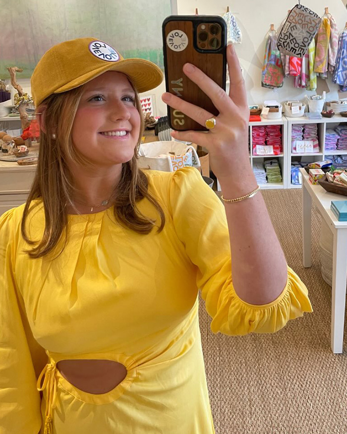 Young woman in yellow dress and cap taking a selfie inside a boutique