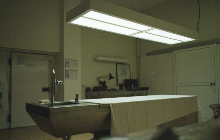 A sterile forensic examination room, with a metal table covered by a white sheet, reflecting the difficult cases lawyers defend.