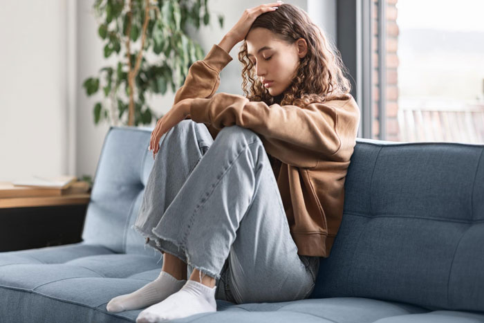 Woman looking upset sitting on couch, reflecting on babysitting challenges Woman looking upset sitting on couch, reflecting on babysitting challenges