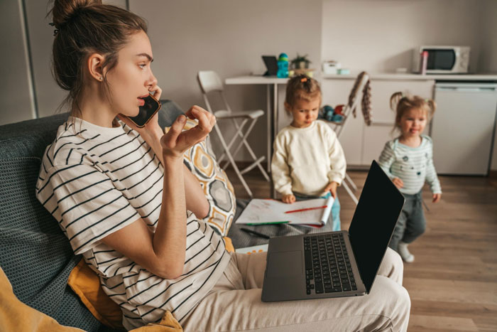 Woman multitasking as babysitter and working on laptop at home with children playing nearby Woman multitasking as babysitter and working on laptop at home with children playing nearby