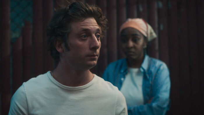 Jeremy Allen White como Carmy em The Bear, parecendo preocupado, com uma mulher desfocada atrás dele. O Urso Temporada 5.