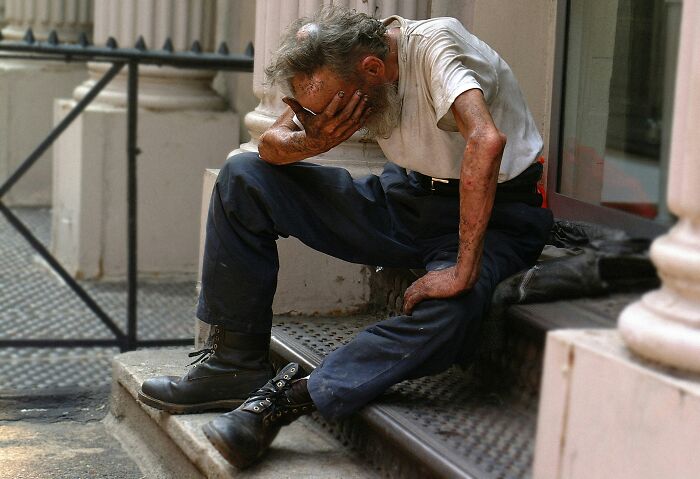 Disheveled man sitting on steps with head in hand showing societal despair