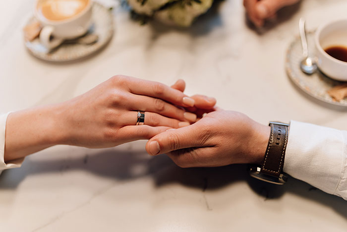 Couple holding hands showing engagement ring on marble table with coffee cups Couple holding hands showing engagement ring on marble table with coffee cups